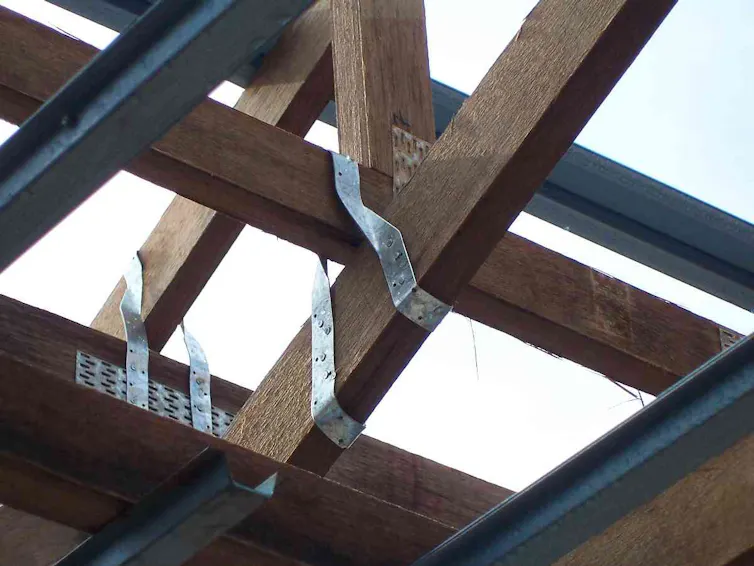 A roof under construction and still open to the sky. Thin metal straps are attached to both roof rafters and walls.