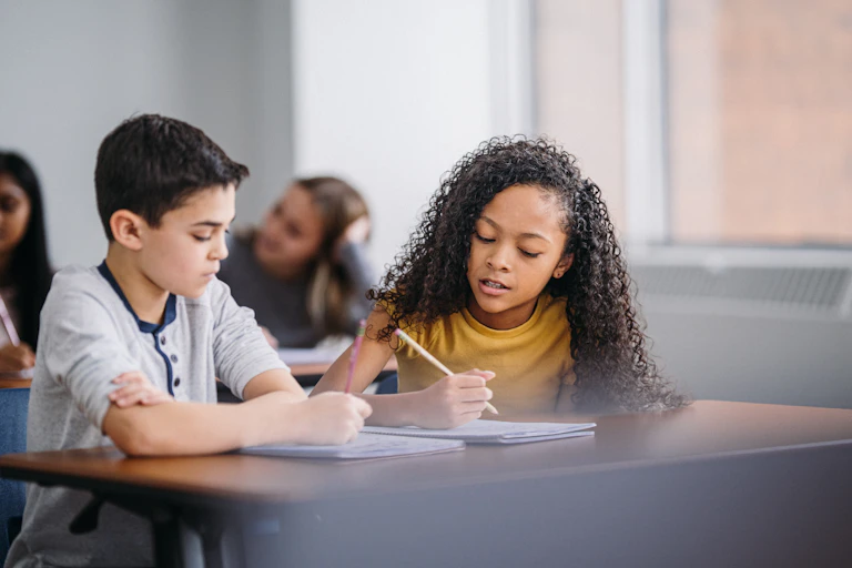 Two middle-school students -- a boy and a girl -- do classwork on a desk.