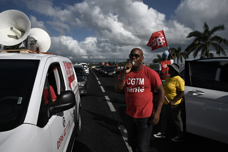 A man speaks into a microphone surrounded by protesters.
