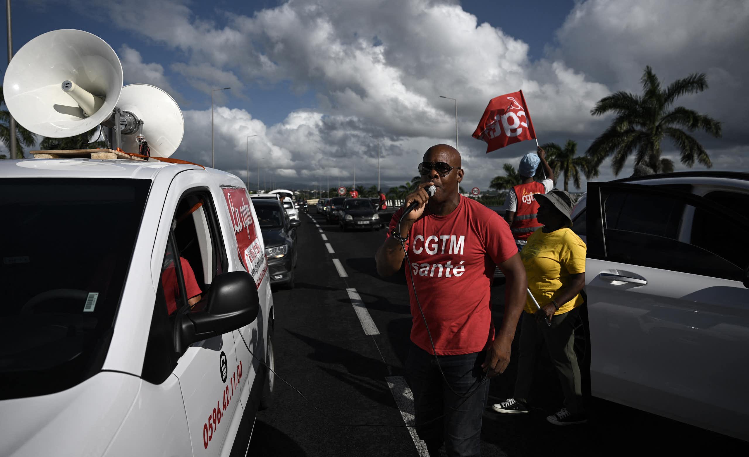 A man speaks into a microphone surrounded by protesters.