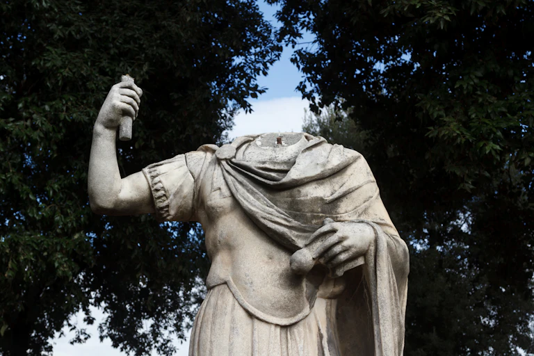 A headless statue stands against a blue sky in Rome.
