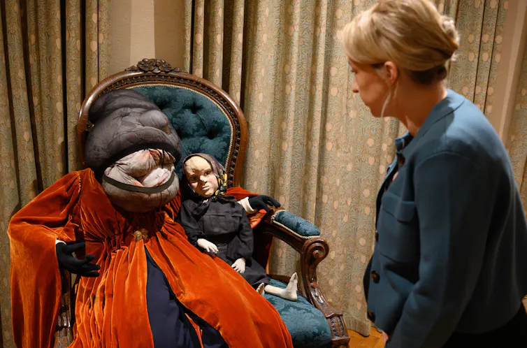 Installation artwork showing a doll and a pillow creature on a chair.