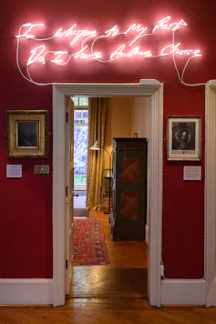 Neon lights spelling 'I Whisper to My Past, Do I have Another Choice' above a doorway.