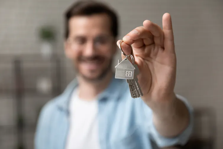 Blurred photo of a smiling man holding out a key to his new home, the key and hand are in focus