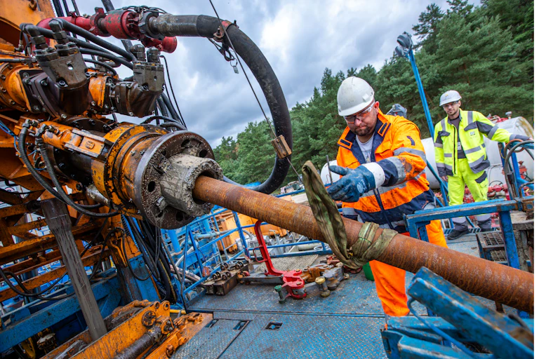 Workers in protective suits and hard hats mount pipe on a drilling rig.