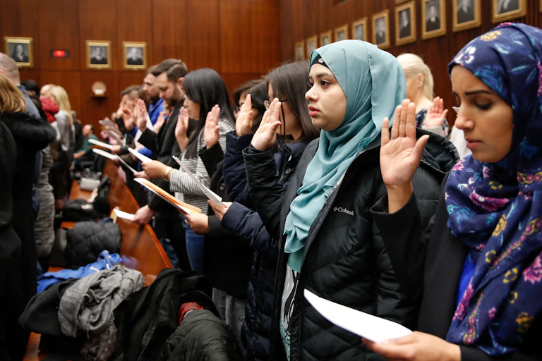 Group of people in courtroom with right hands raised taking naturalization oath.