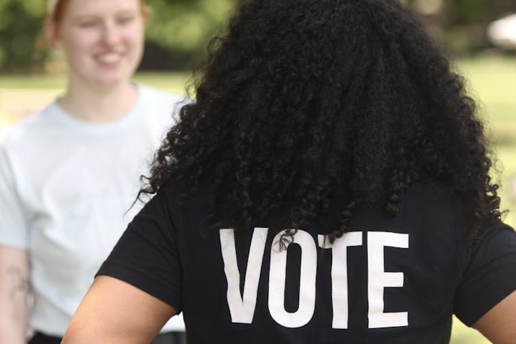 woman faces away from camera, wearing a 'VOTE' t shirt