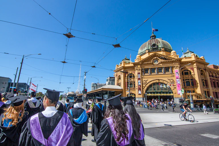 A group of graduates in robes and mortar boards walk near Flinders St station in Melbourne.