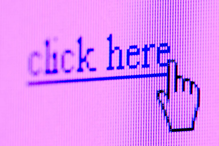 Photo of a pixelated computer screen showing a hand cursor hovering over hyperlink text reading 'click here'.