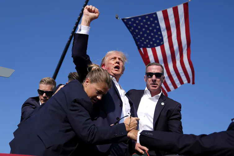 Trump raises a fist, the flag behind him.
