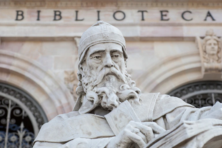 Stone statue of old, bearded man wearing religious robes and holding large booklet.