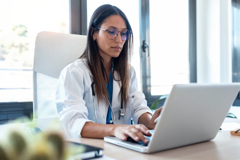 A female doctor types on her laptop.