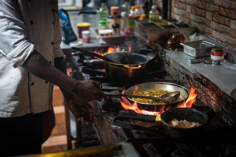 A man cooks four pans of food over gas