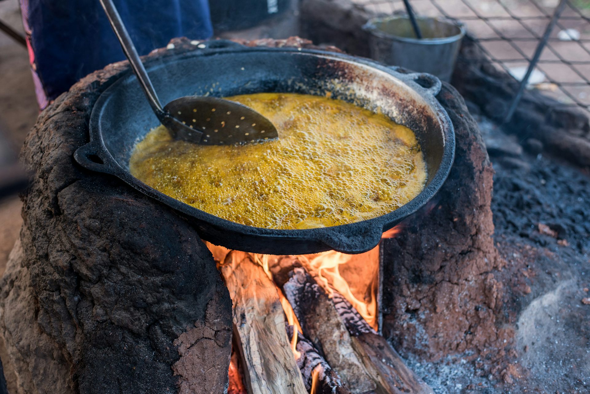A pot balanced on large stones over a fire where bean cakes are frying in oil