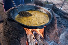 A pot balanced on large stones over a fire where bean cakes are frying in oil