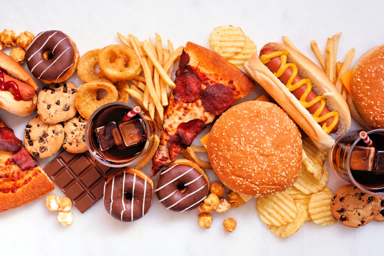 Collection of take out and fast foods. Pizza, hamburgers, french fries, chips, hot dogs, sweets.