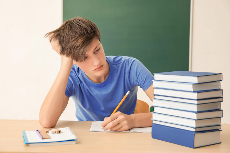 Un garçon qui écrit et une pile de livres
