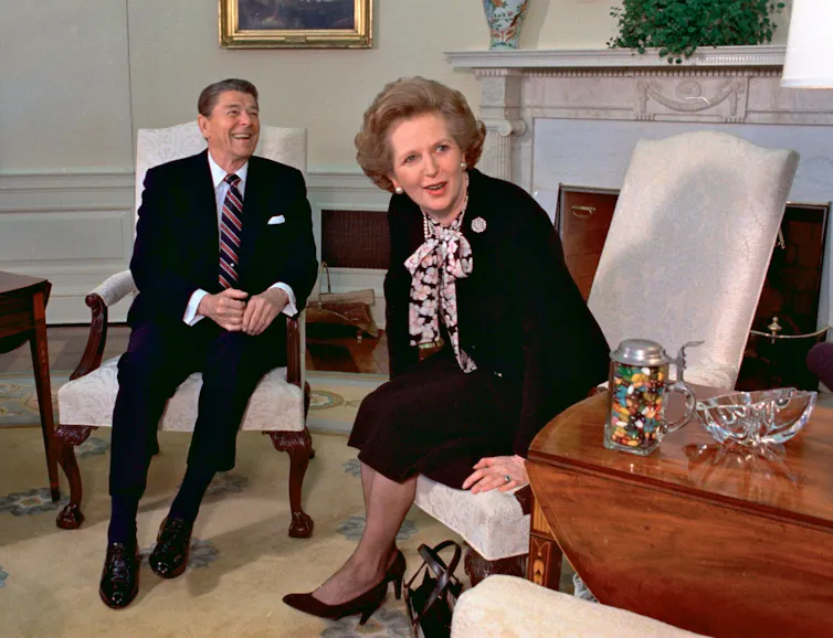 Margaret Thatcher and Ronald Reagan laughing on chairs in the White House.