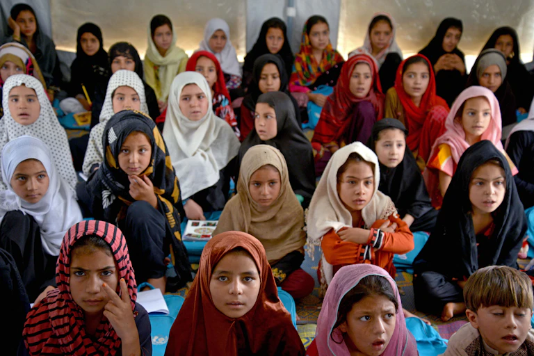 A classroom of Afghan students -- mostly girls with headscarves -- sit on a floor in an Afghan school.
