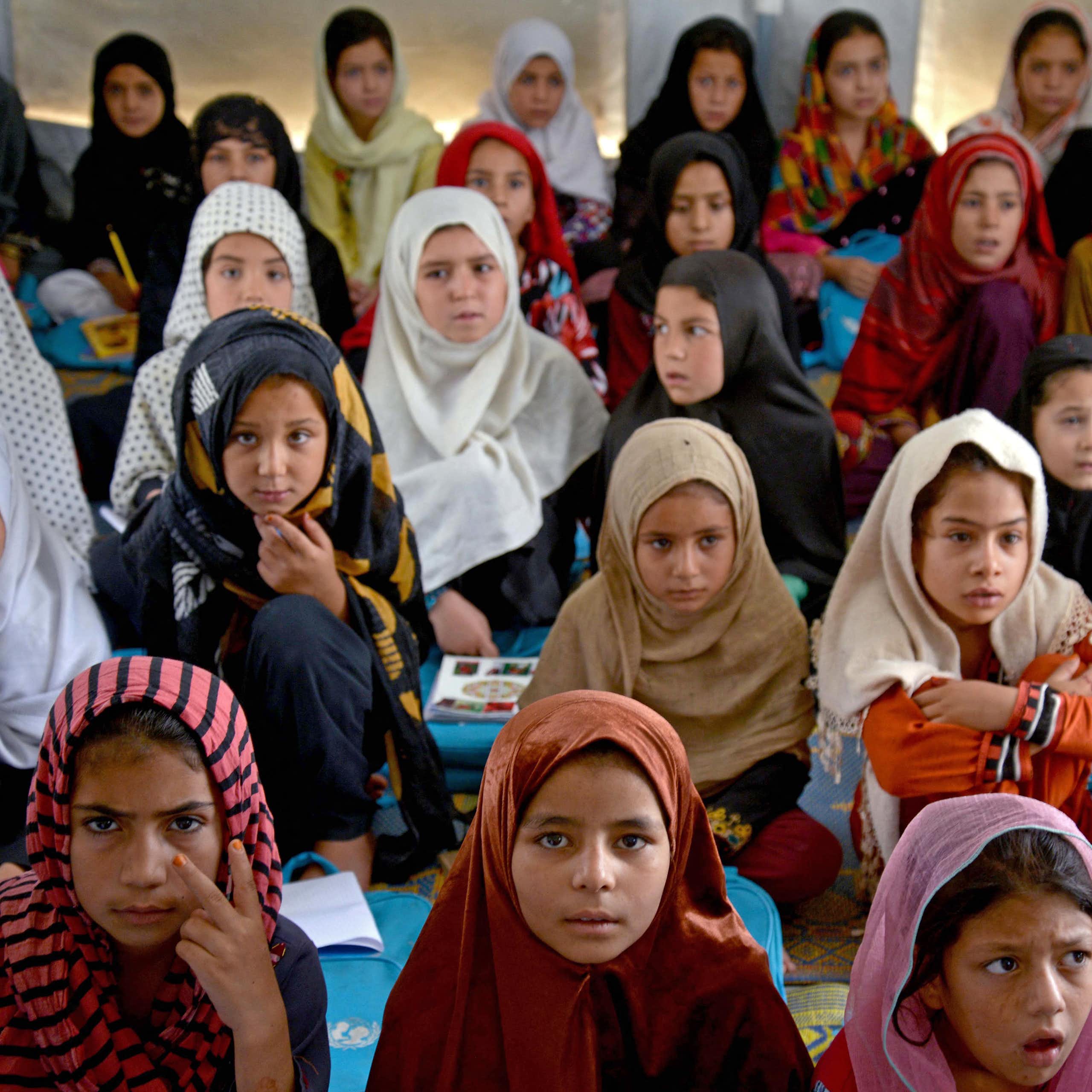A classroom of Afghan students -- mostly girls with headscarves -- sit on a floor in an Afghan school.