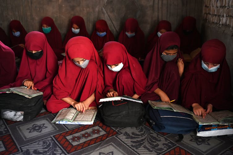 Young girls in red overgarments and head coverings read passages from the Qur'an.