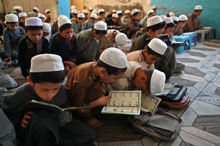 Boys with skullcaps read passages from the Qur'an.