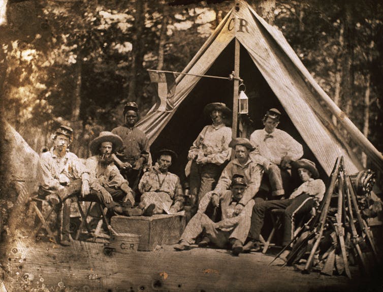 A historic, sepia-toned photo of Confederate soldiers posing for a photo outside their tent.