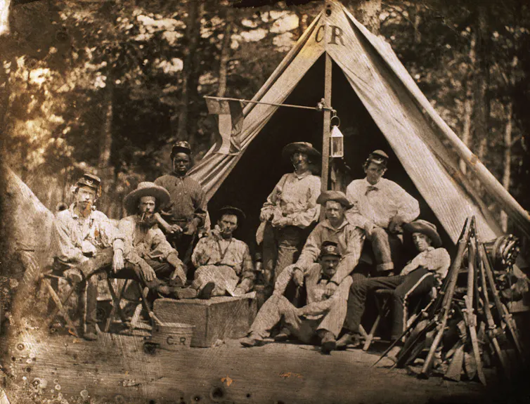 A historic, sepia-toned photo of Confederate soldiers posing for a photo outside their tent.