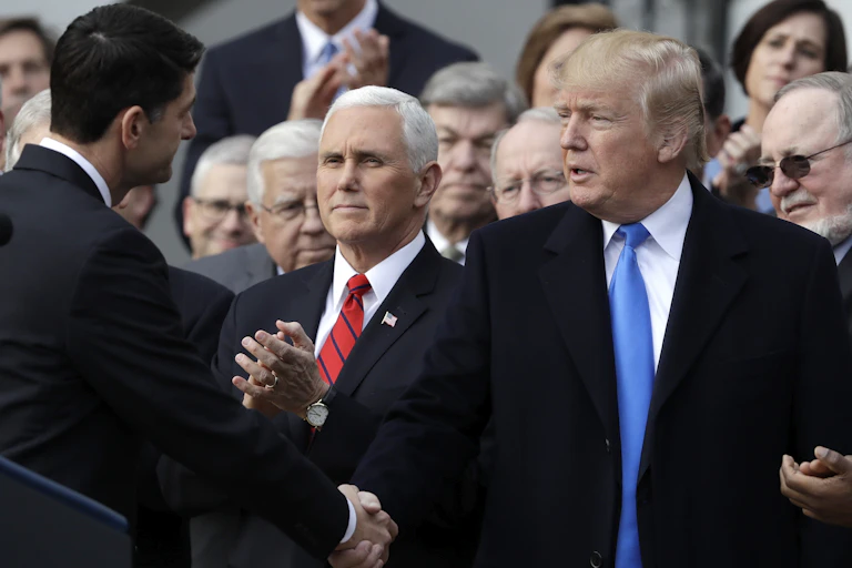 Donald Trump shakes hands with a man with dark hair while Mike Pence stands by his side amid a crowd of lawmakers.