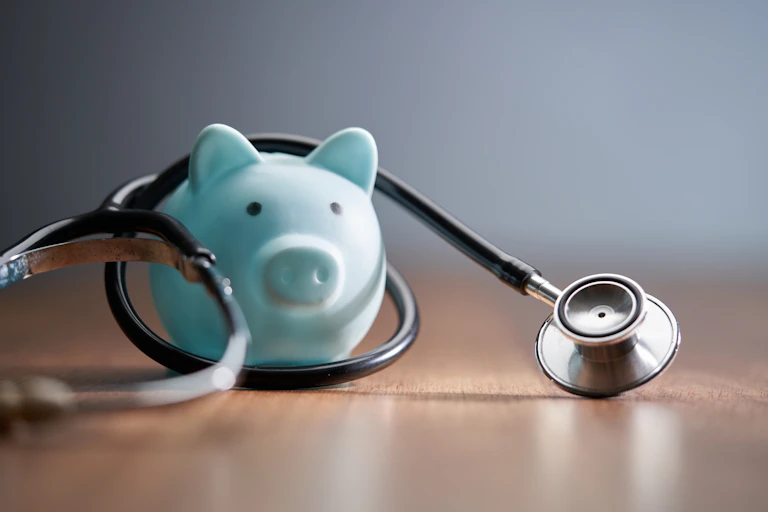 stethoscope and blue piggy bank on wood table top