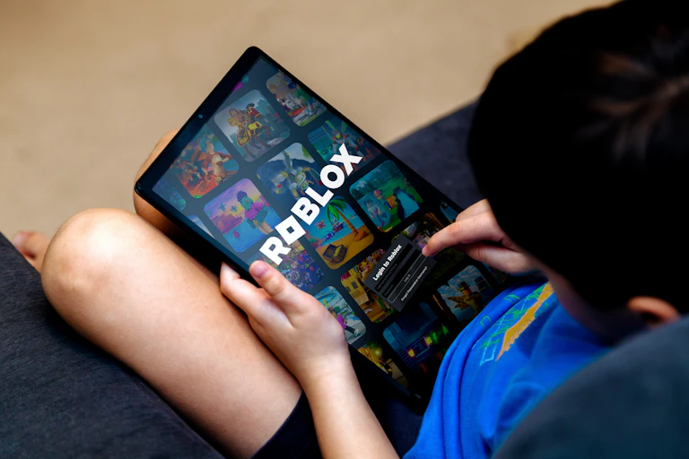 Young boy sitting on a couch playing Roblox on a computer tablet.