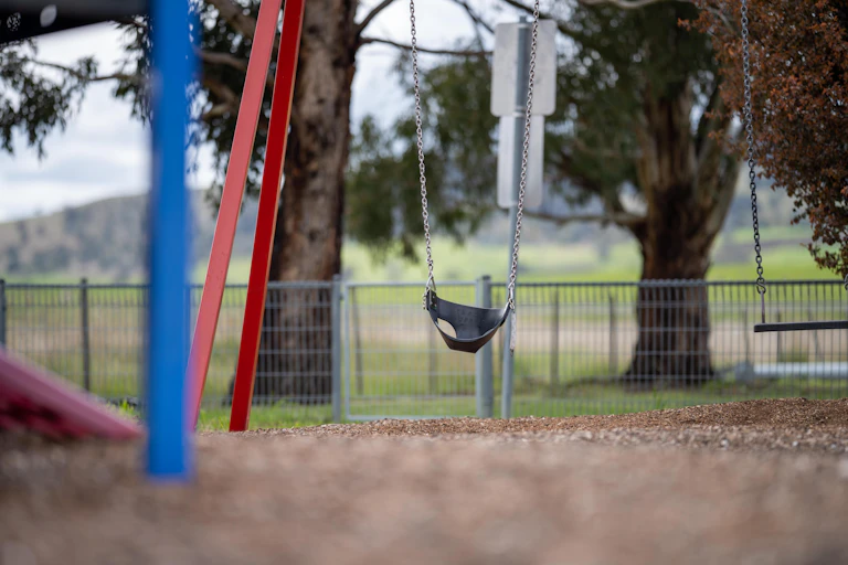 An empty swing set with trees and grass in the background.