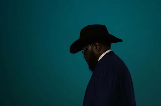 Profile of a man wearing a dark hat, with spectacles and a beard