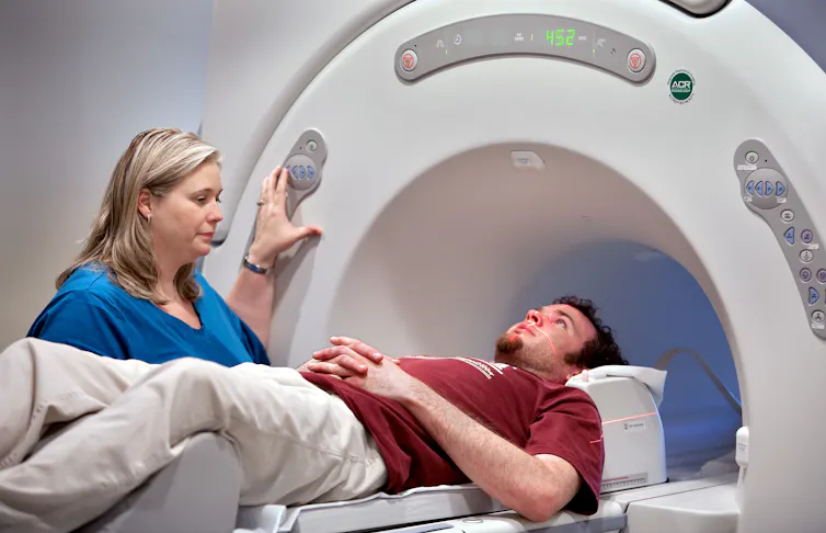 A man about to enter an MRI scanner. A medic stands to one side.