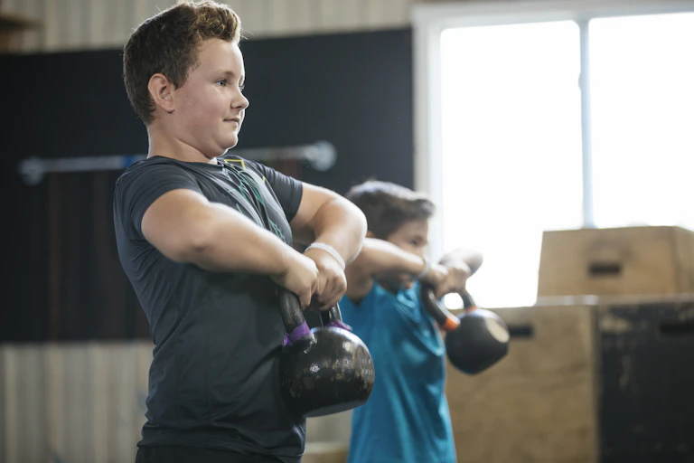 Two boys lifting kettlebells.
