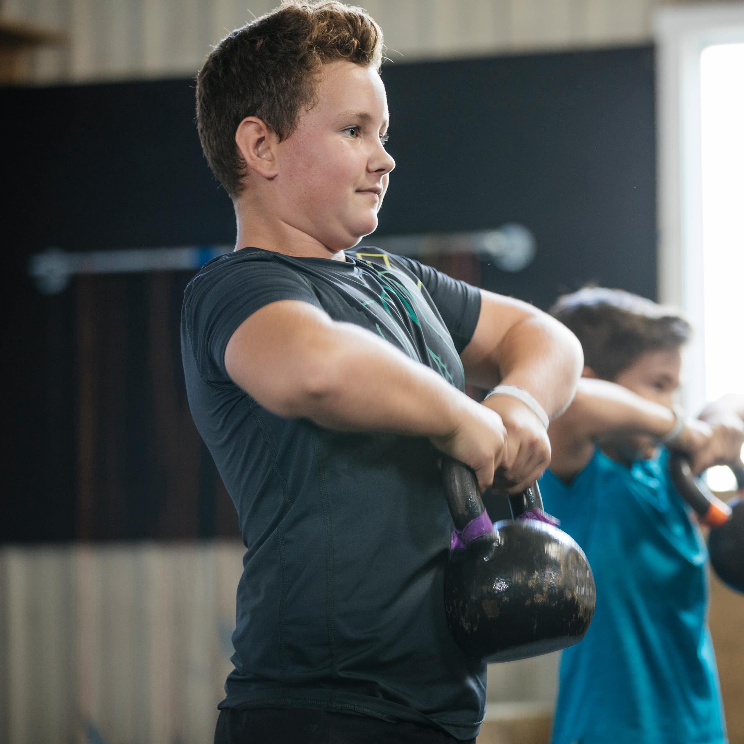 Two boys lifting kettlebells.
