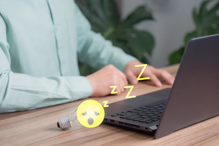 Man working on laptop with sleepy lightbulb cartoon.