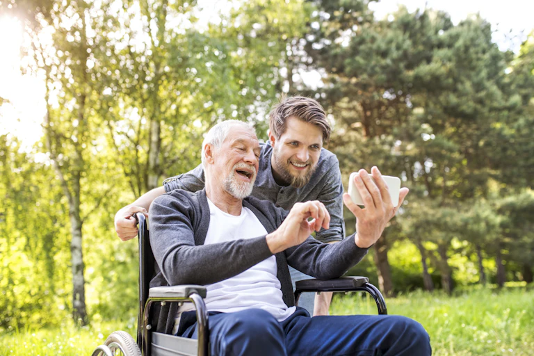 Older man in wheelchair looks at phone with younger man