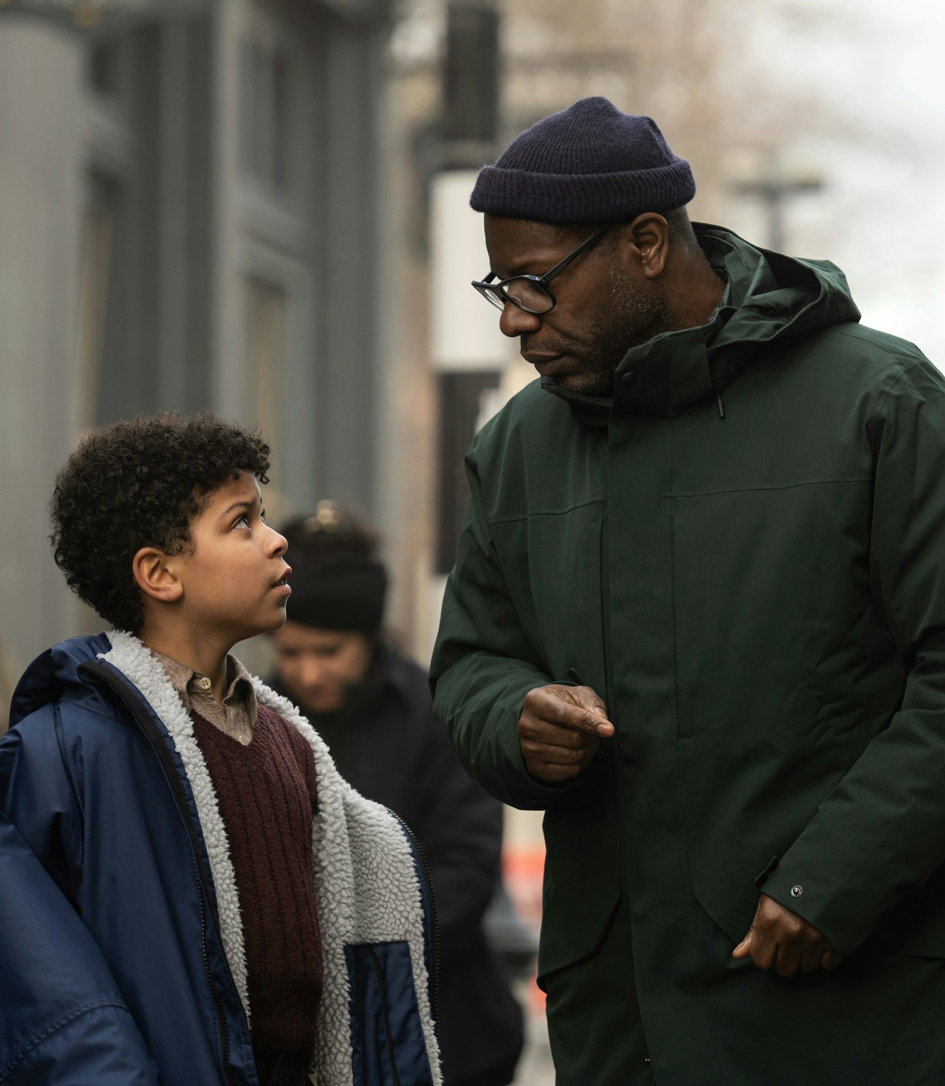 A man in a parka and beanie directing a young boy on a film set.