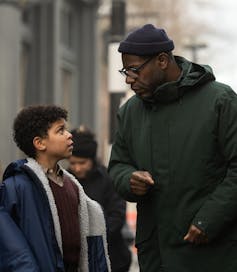 A man in a parka and beanie directing a young boy on a film set.