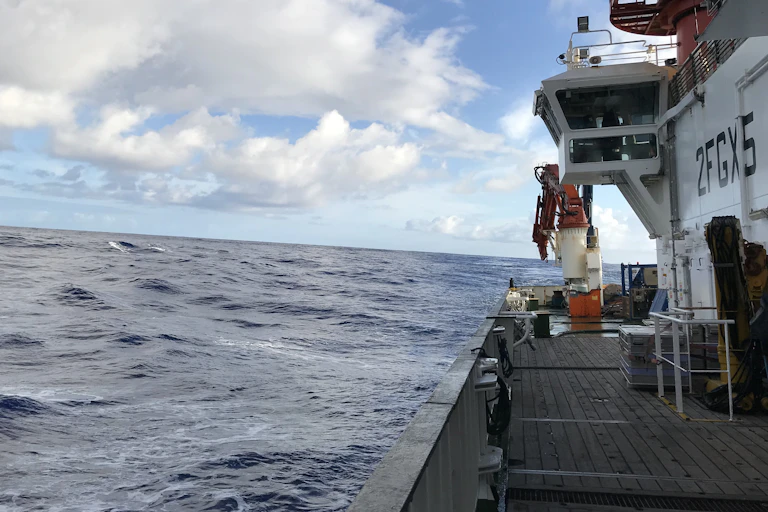 side of research ship and wavy sea, blue sky with clouds