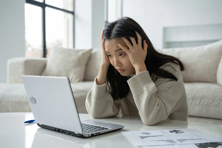 Woman with head in hands staring at laptop.