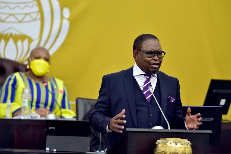 A man wearing a three piece suit and tie speaks at a podium.