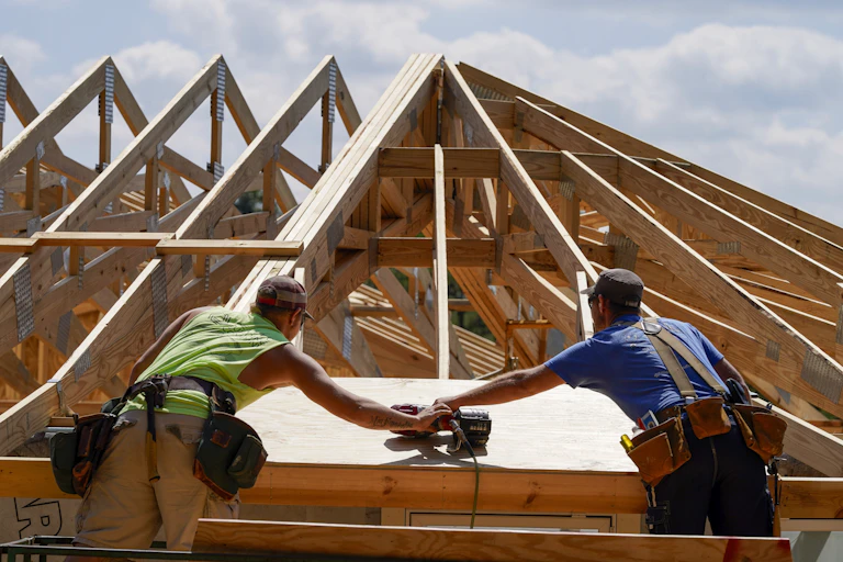 Two construction workers work on the roof of a home. It has a curve design to stand up to wind.