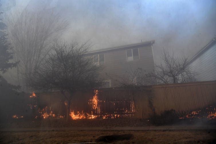Flames rise along a fence behind a home.