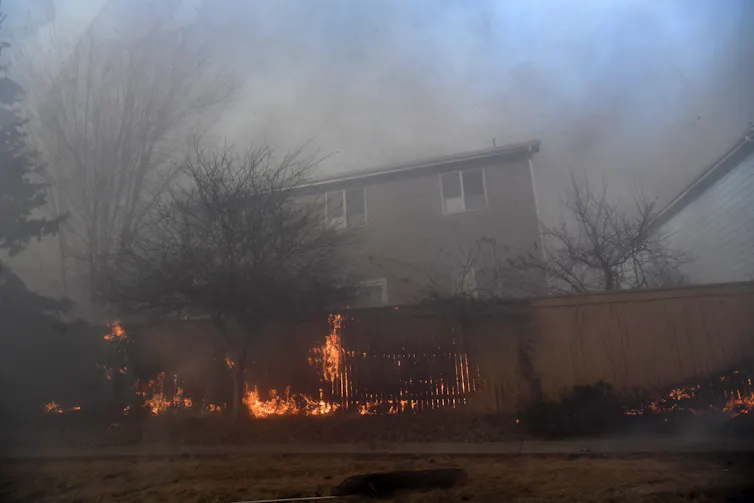 Flames rise along a fence behind a home.