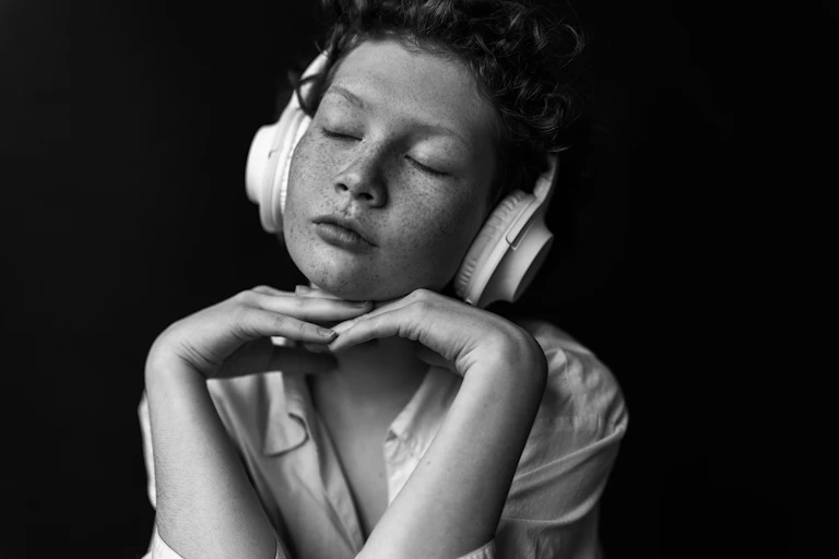 Black and white portrait of person listening to music with eyes closed, headphones on, chin resting on cradle of hands