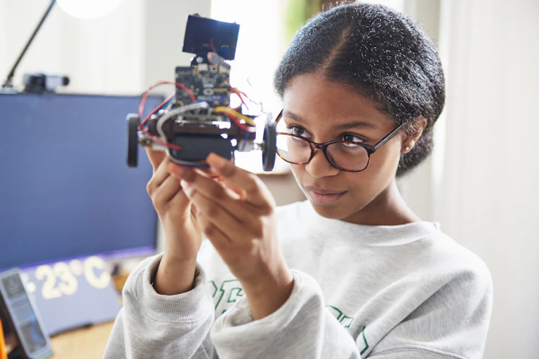 Black girl holding robot looks at it carefully