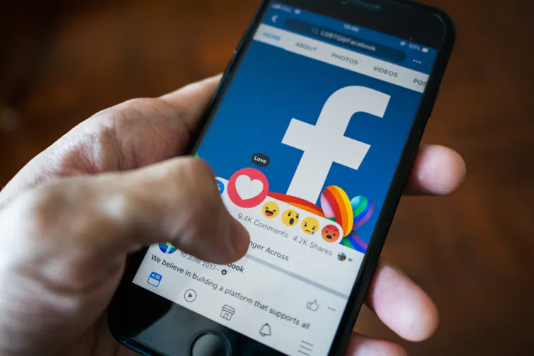 Photo of a person's hand holding a phone showing Facebook.