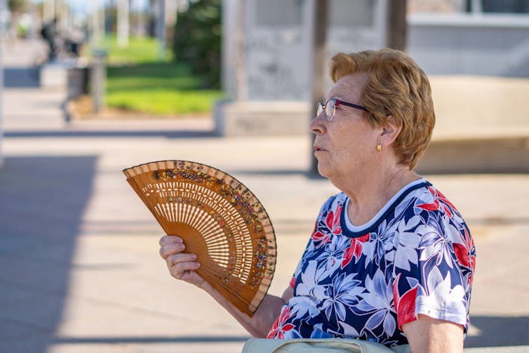 A senior woman outdoors using a fan.